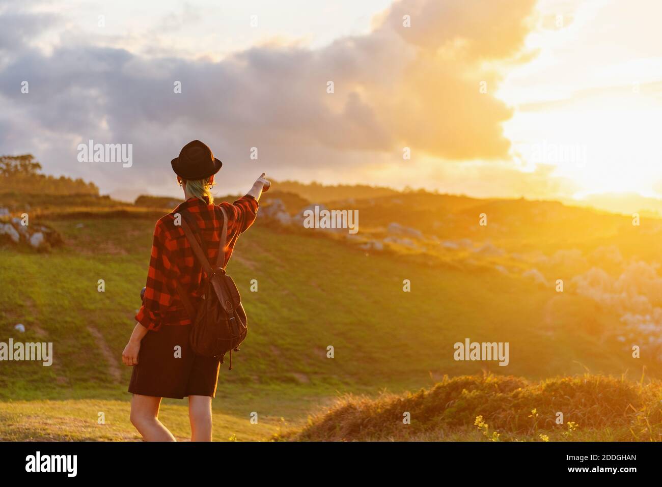 Vista posteriore di esploratore anonimo in camicia a scacchi in piedi hill e puntando via al cielo del tramonto durante il viaggio estivo Foto Stock