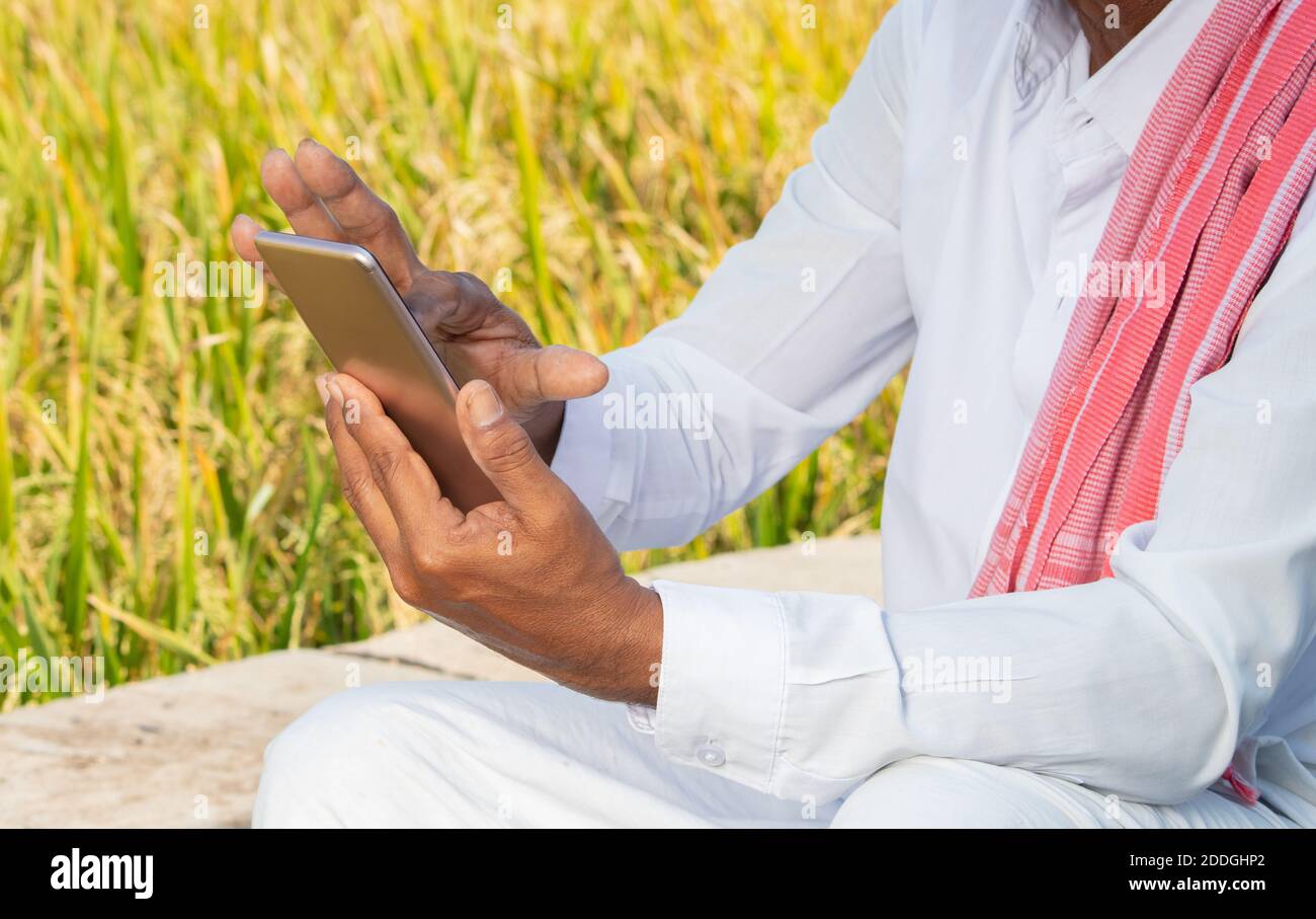 Primo piano di mani di carestia indiana utilizzando mobile vicino agricolo Fattoria terra - anziani hsnds villager utilizzando il telefono - concetto di gente rurale anziana usando Foto Stock