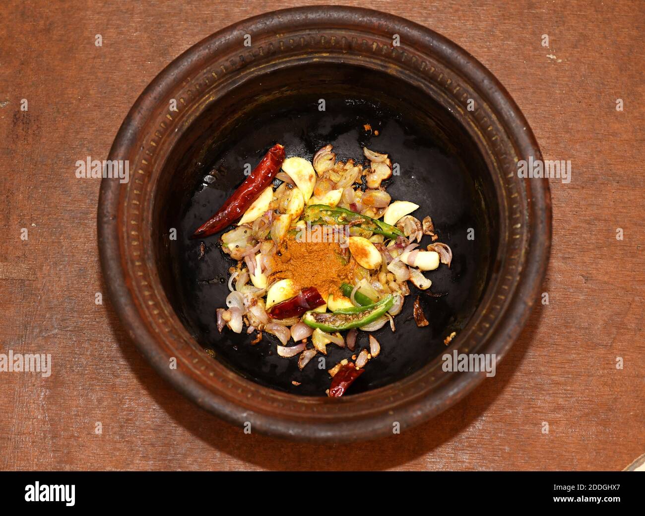 Saltando o saltando in una padella di fango aglio, curcuma, cipolle, peperoncino verde e senape in olio in un piatto di fango.cucina indiana del sud ricette. Foto Stock