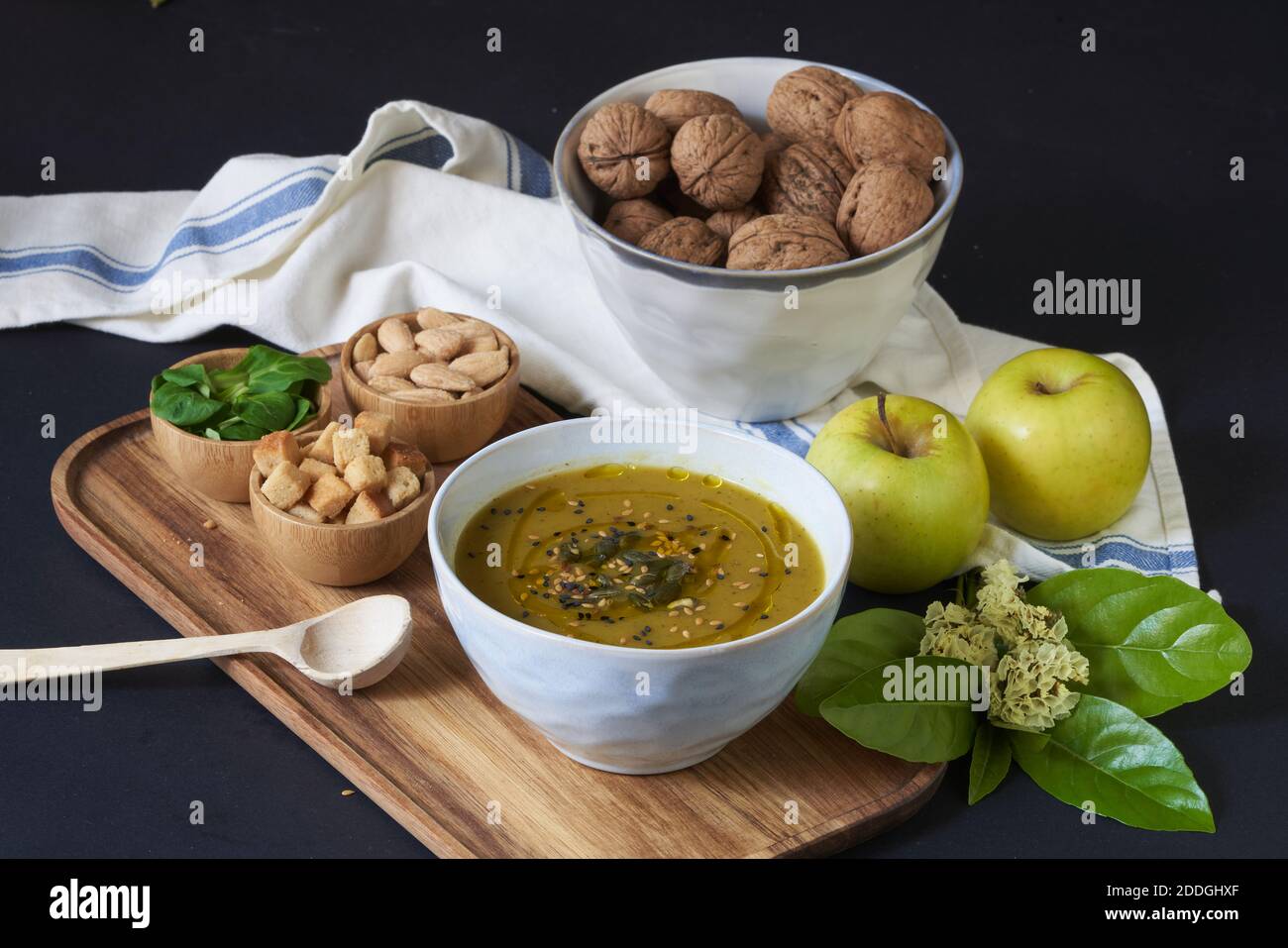 Dall'alto di gustosa zuppa di crema vegana con semi di zucca sistemato su vassoio di legno con crostini di pane e basilico fresco posto sul tavolo vicino alle mele e wa Foto Stock