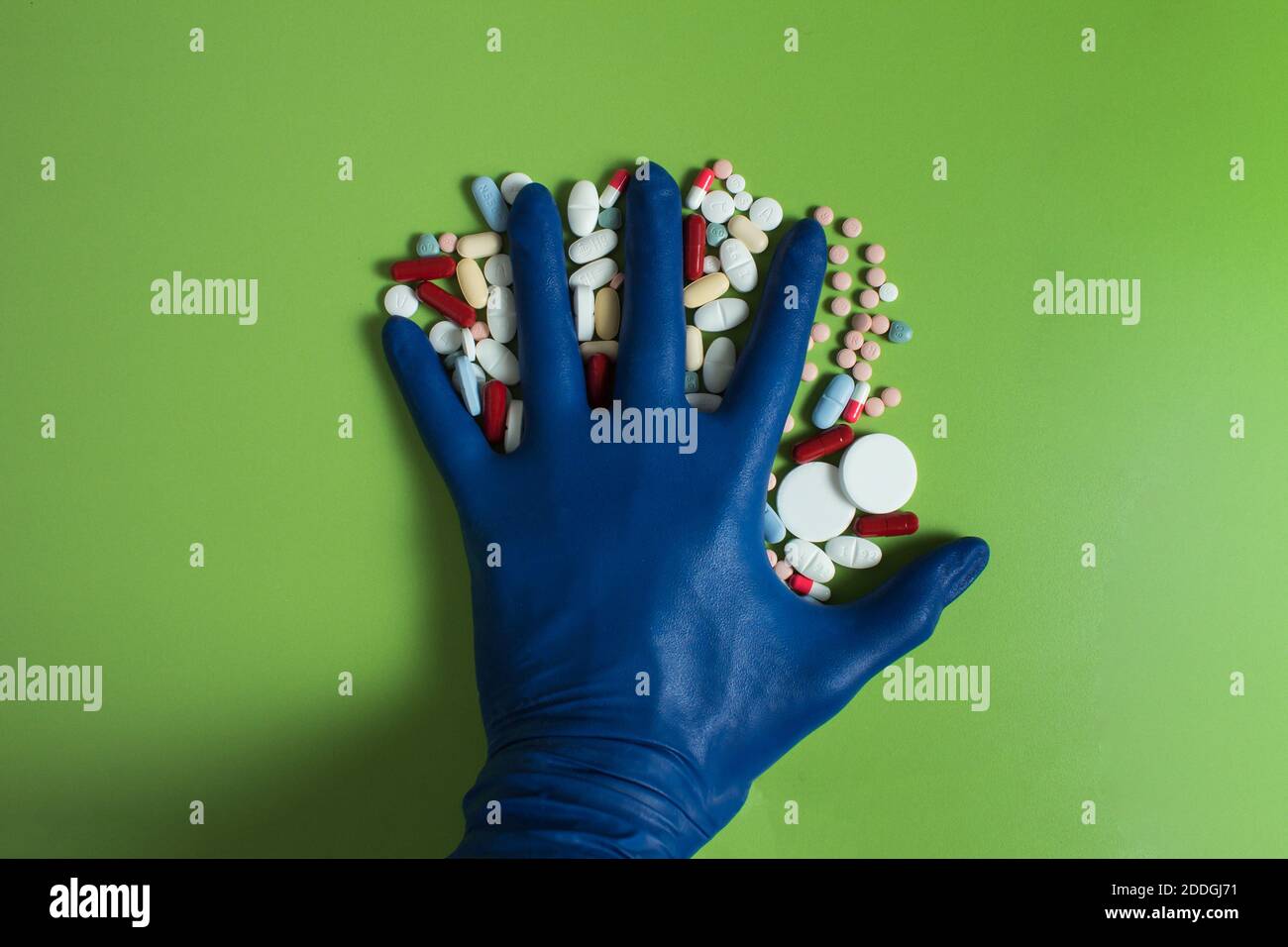 Diverse pillole e capsule tra le dita di una faccia aperta verso il basso mano protetto con un guanto blu su un tavolo verde. Foto Stock