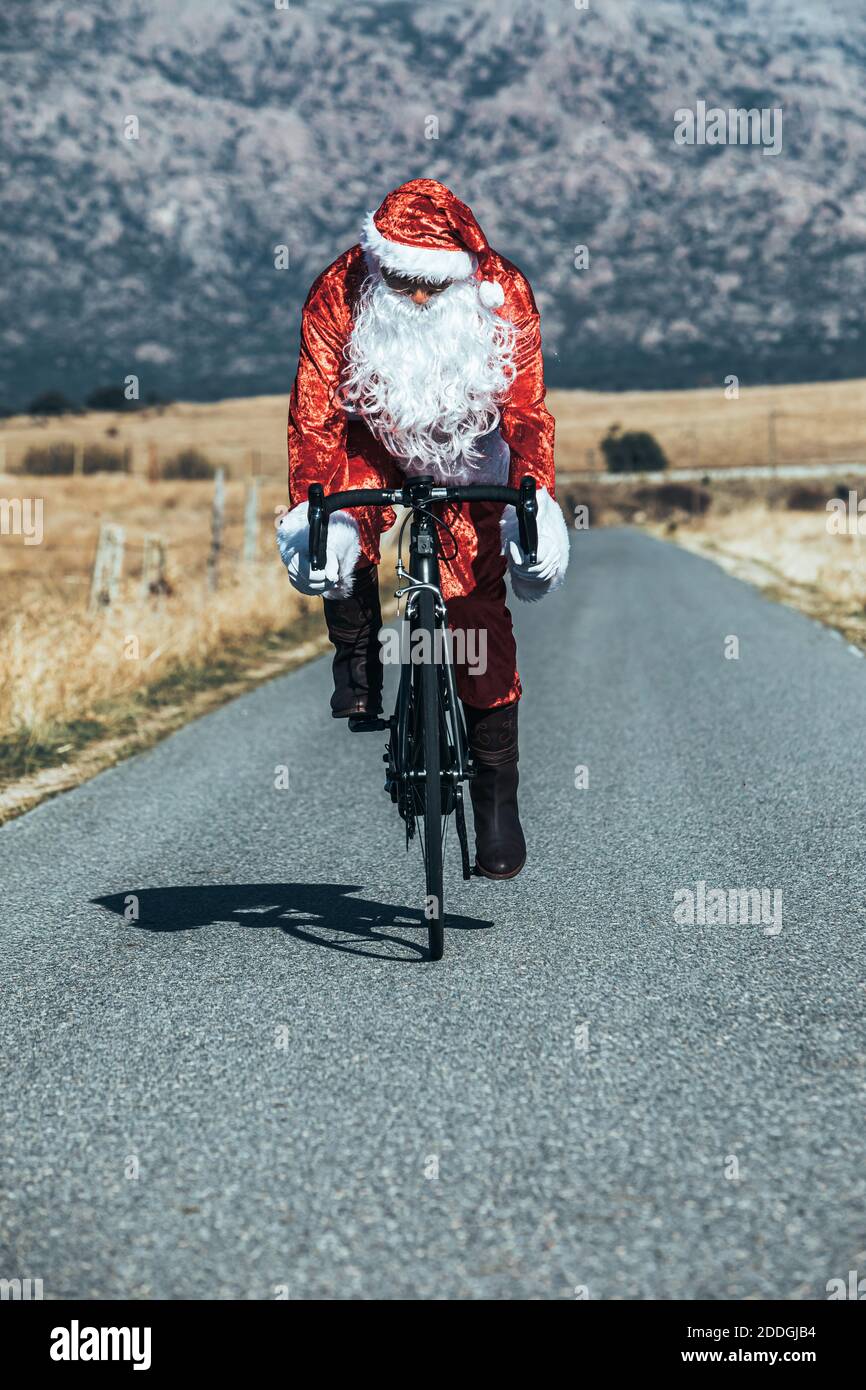 Babbo Natale in costume rosso in bicicletta moderna lungo vuoto strada in altopiani in giornata di sole Foto Stock