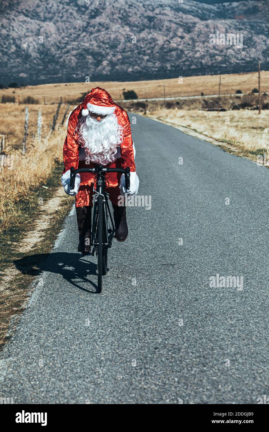 Babbo Natale in costume rosso in bicicletta moderna lungo vuoto strada in altopiani in giornata di sole Foto Stock