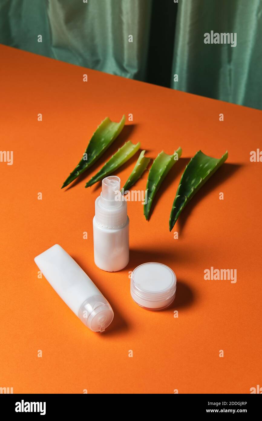 Vista dall'alto dei prodotti per la cura della pelle del viso in plastica bianca vasi e foglie di aloe vera pianta posto su arancio sfondo in studio Foto Stock