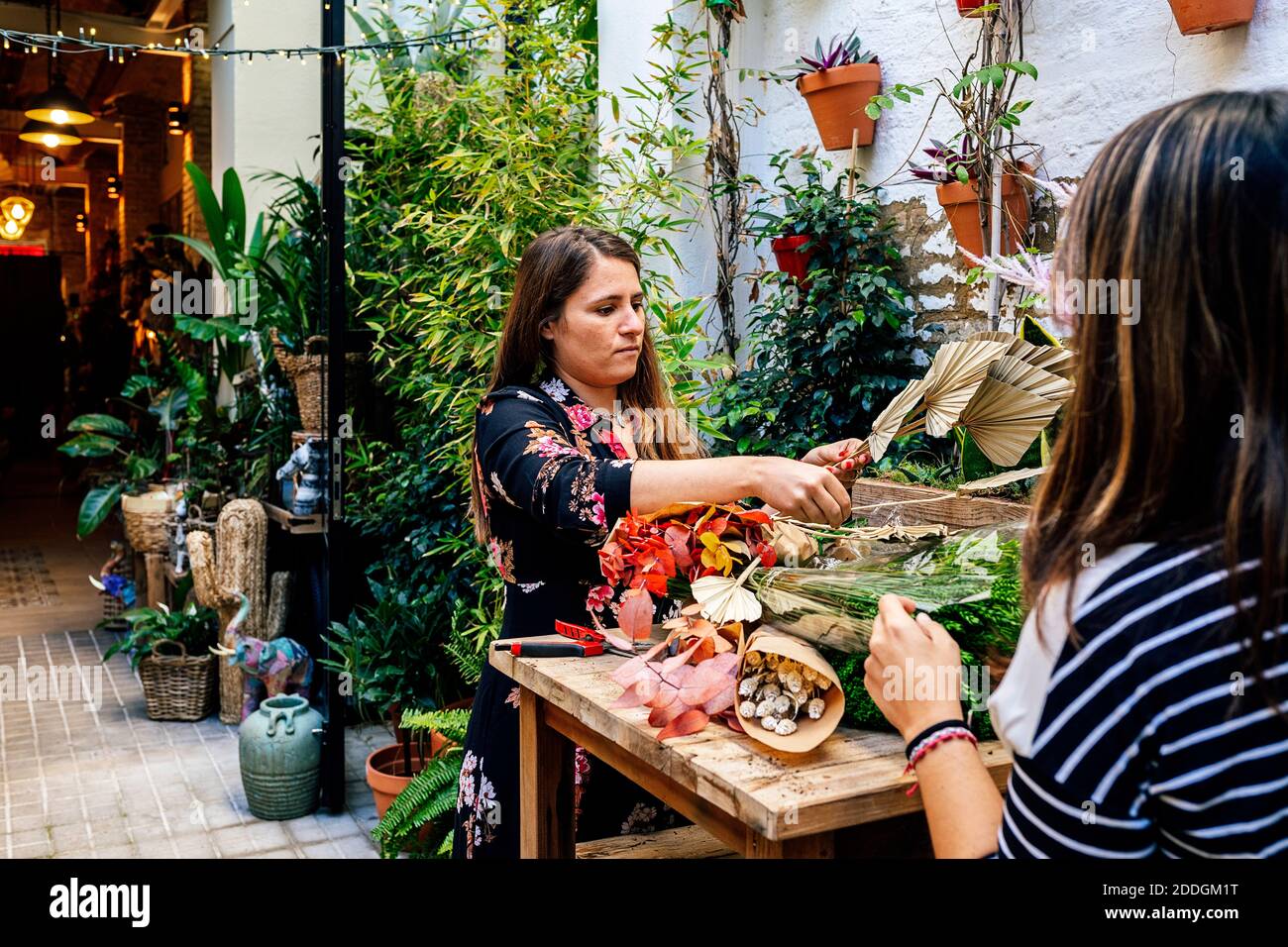 Fioristi professionisti che organizzano bouquet di fiori mentre lavorano insieme negozio seduto su tavolo di legno Foto Stock