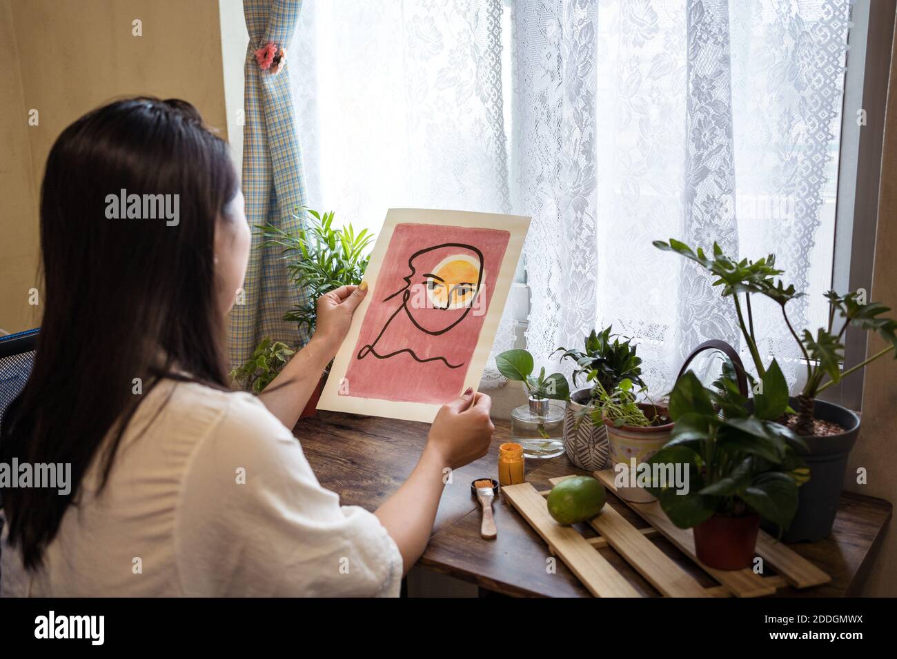 Dall'alto, vista posteriore dell'artista femminile asiatica che riflette specchio seduto al tavolo e ammirando opere d'arte incredibili Foto Stock