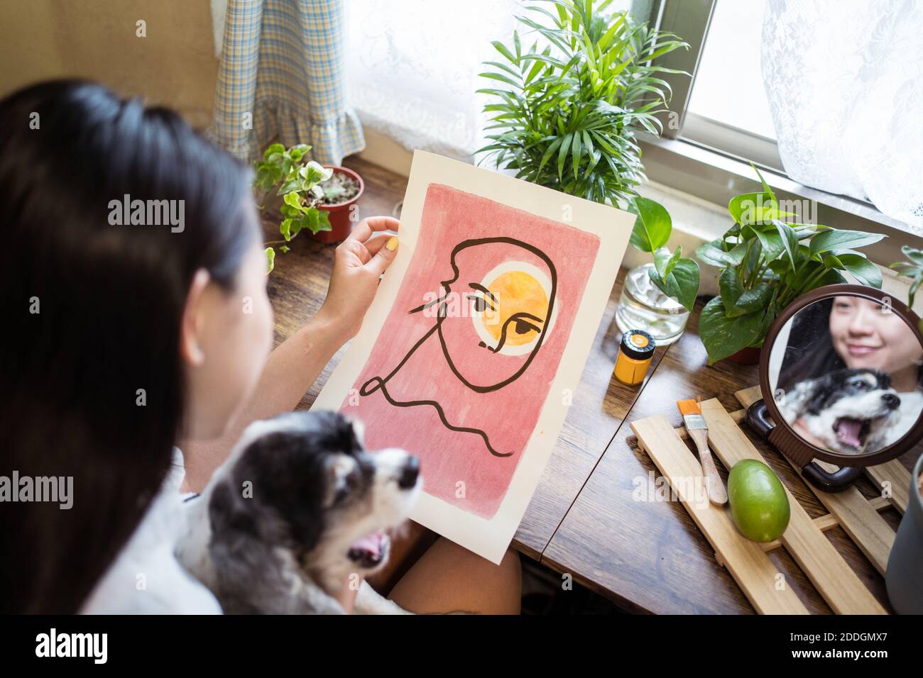 Dall'alto di sorridente artista femminile asiatica riflettendo nello specchio seduto al tavolo e ammirando opere d'arte straordinarie Foto Stock