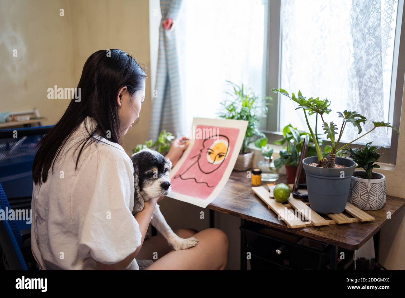 Dall'alto di sorridente artista femminile asiatica riflettendo nello specchio seduto al tavolo e ammirando opere d'arte straordinarie Foto Stock