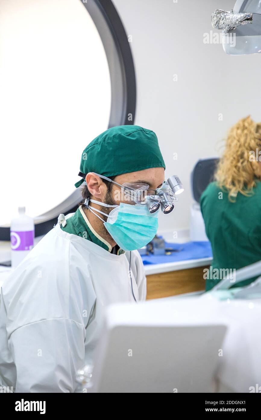 Basso angolo di dentista maschile focalizzato in occhiali binoculari e. lavoro uniforme in moderna clinica dentale Foto Stock
