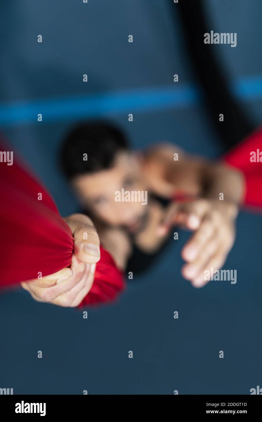 Messa a fuoco morbida dell'uomo che afferra e arrampica su pezzo di tessuti mentre si pratica la danza aerea in studio Foto Stock