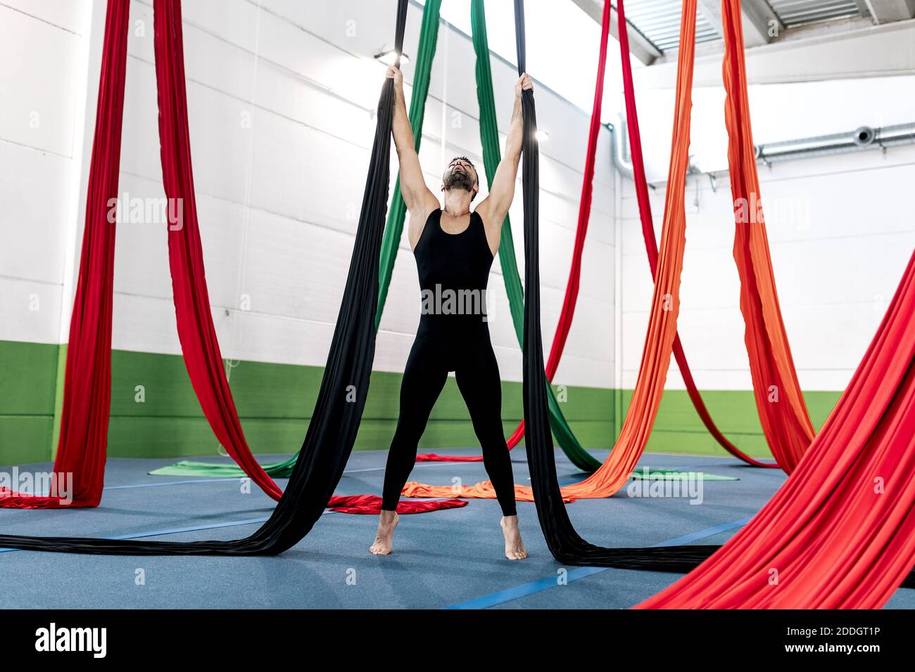 Da sotto a piedi nudi uomo sopportato equilibrando su pezzi di tessuto e guardando verso il soffitto mentre si pratica la danza aerea in studio Foto Stock