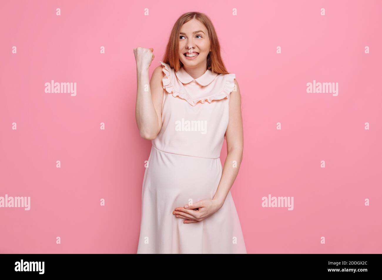 Donna in gravidanza felice gioisce e tiene il ventre su sfondo rosa Foto Stock