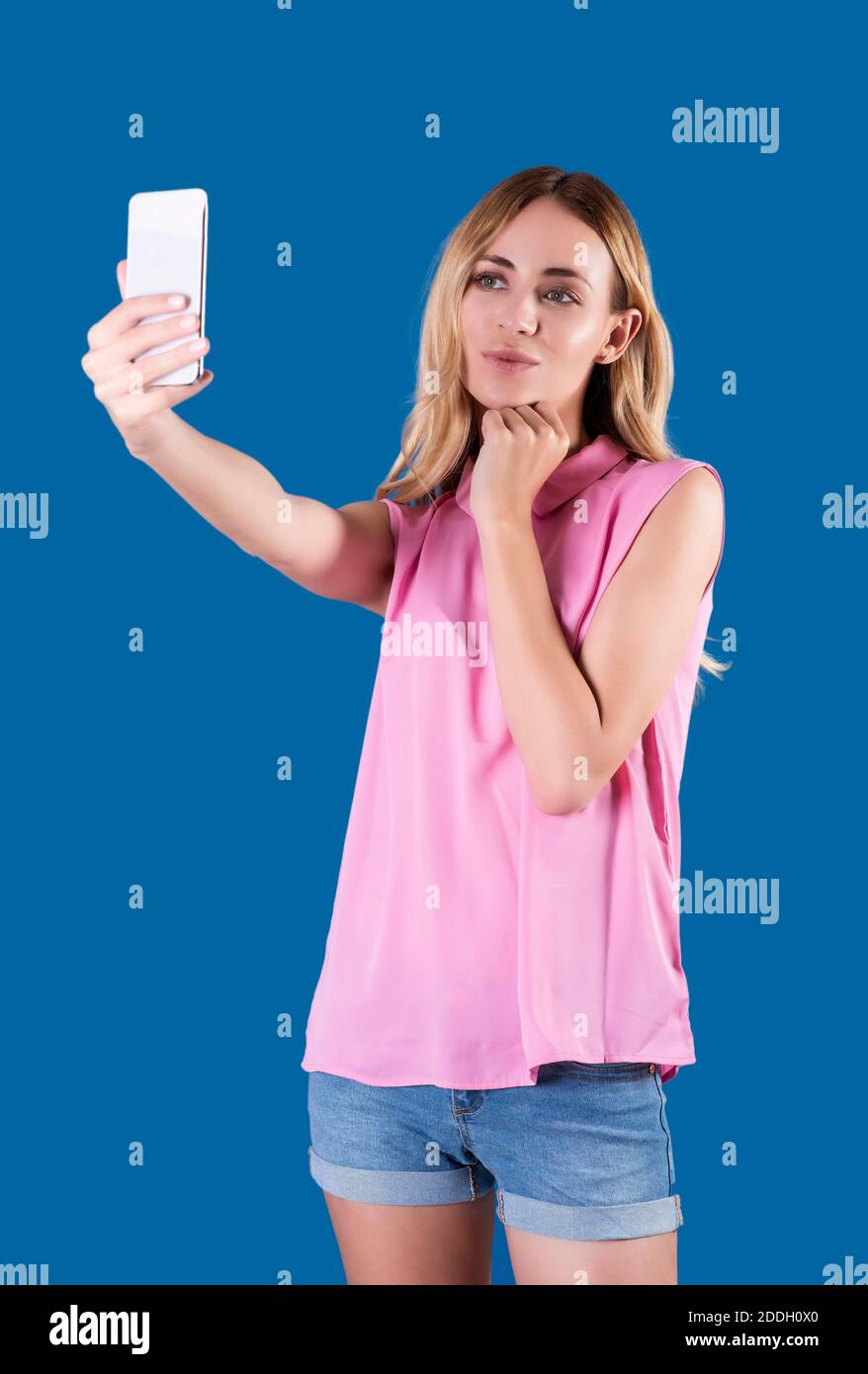 Ragazza bionda che indossa una blusa rosa e shorts jean, prendendo un selfie. Foto Stock