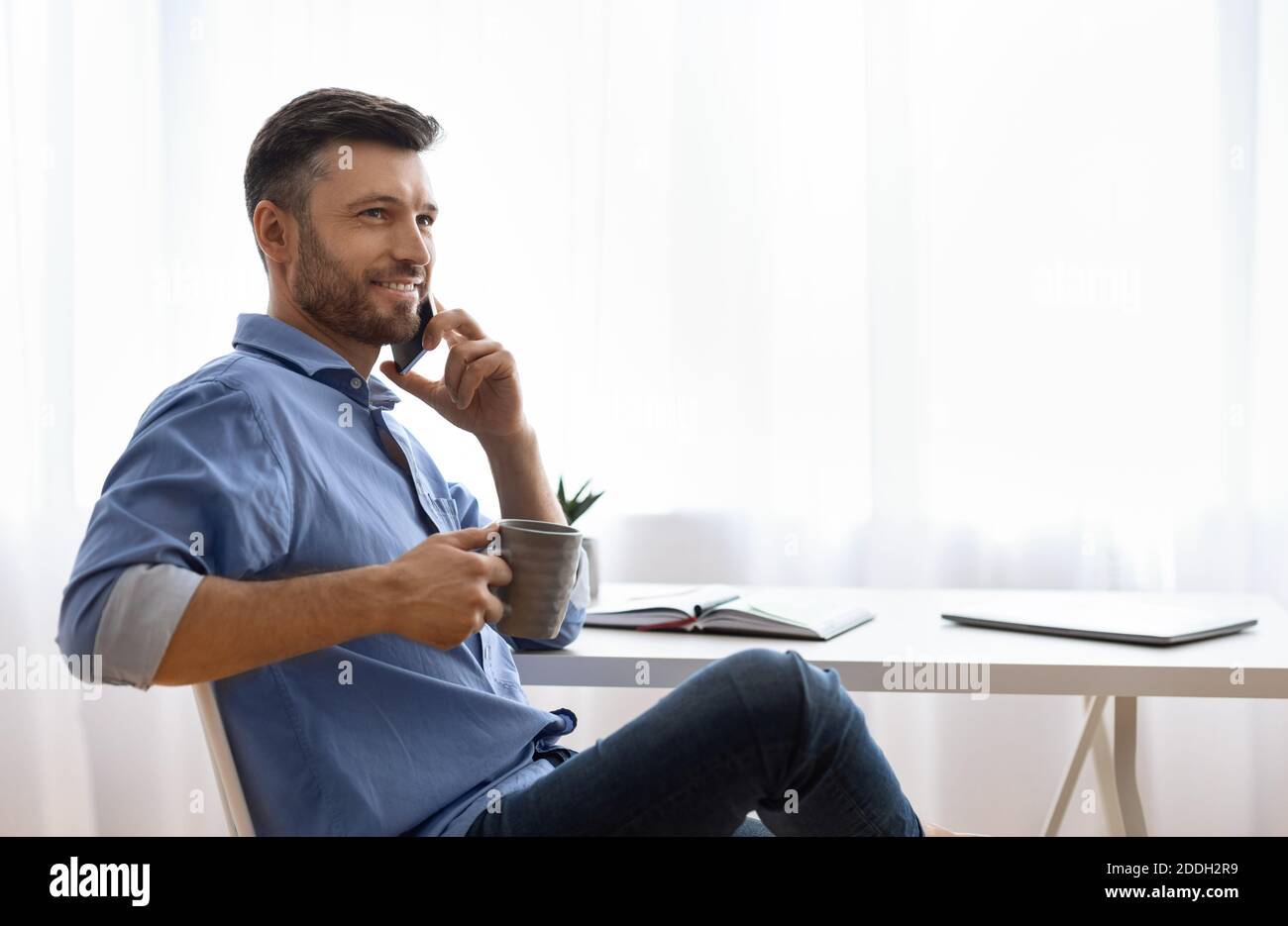 Bell'uomo freelance che parla sul cellulare e beve caffè a. casa Foto Stock