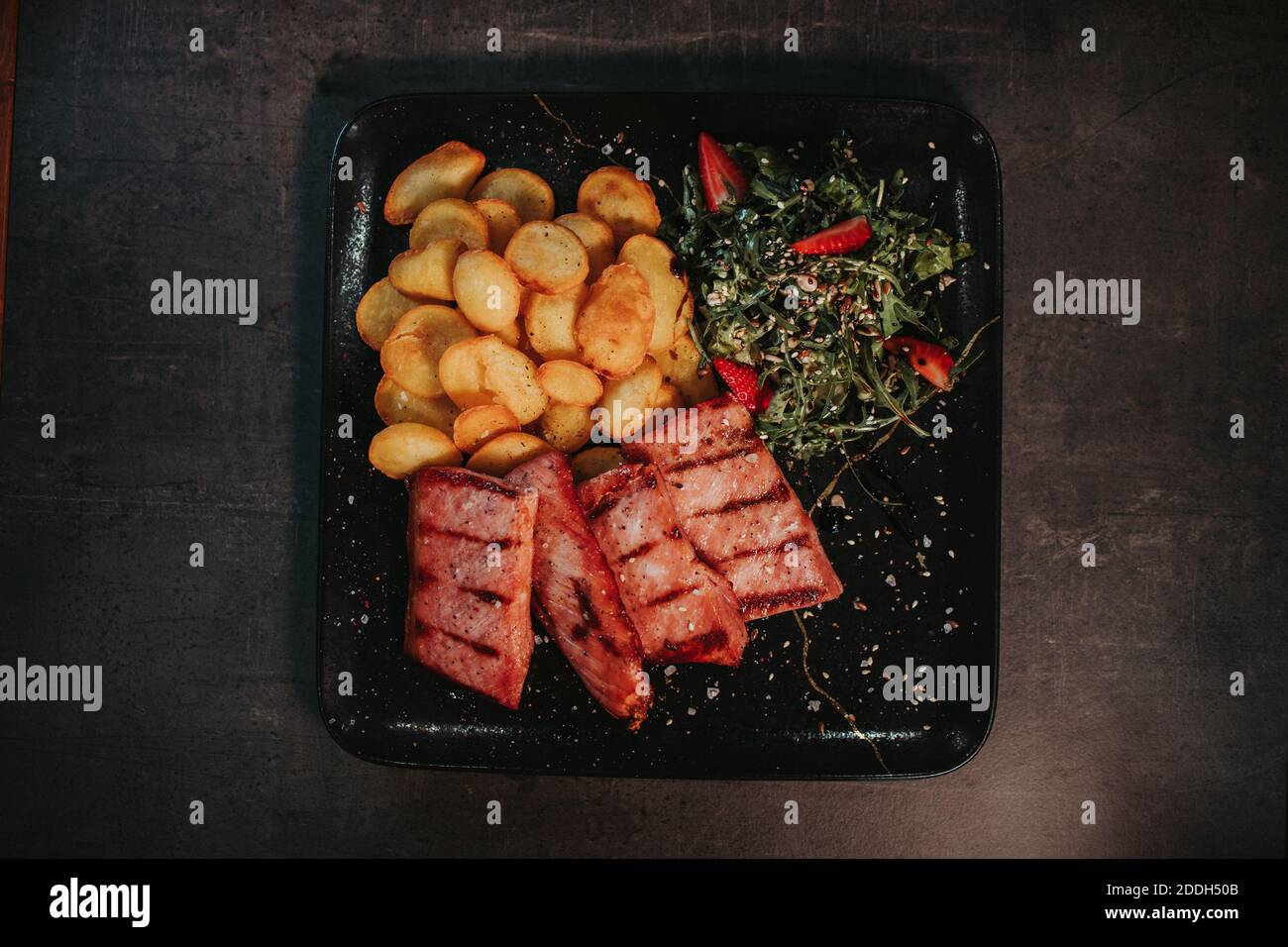 le bistecche di patate al forno e un'insalata verde di foglie una piastra nera Foto Stock