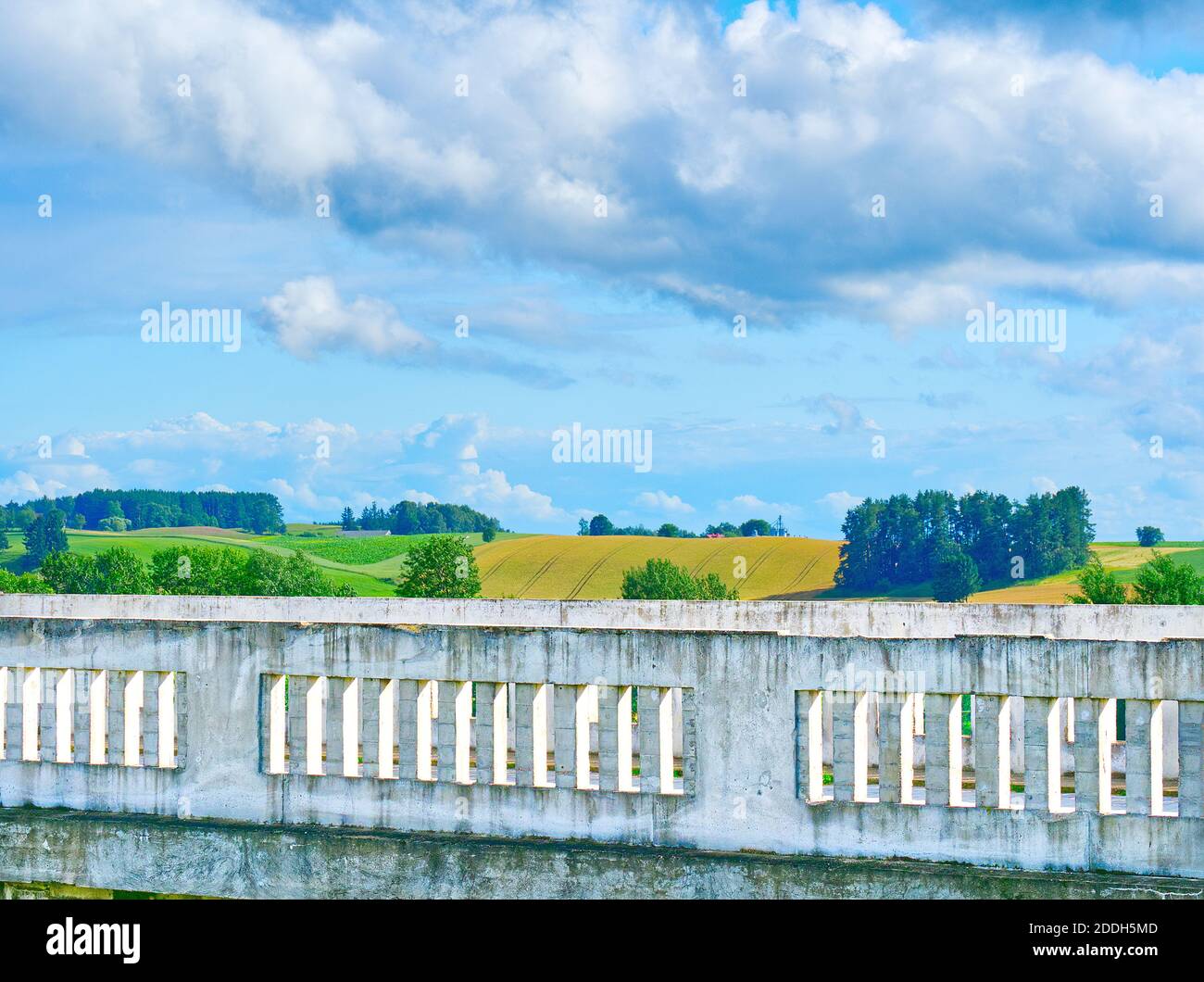 Paesaggio con un mix di elementi architettonici - ringhiere e campi colorati su una collina in secondo piano con cielo azzurro chiaro con nuvole. Foto Stock