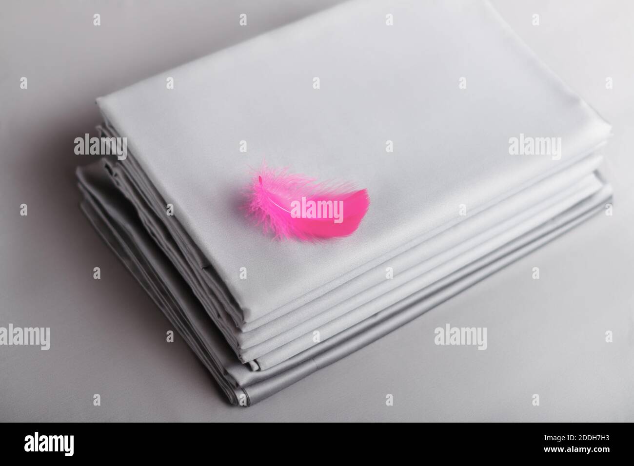 Vista dall'alto di una pila di lenzuola piegate di colore grigio con una piuma rosa. Foto Stock