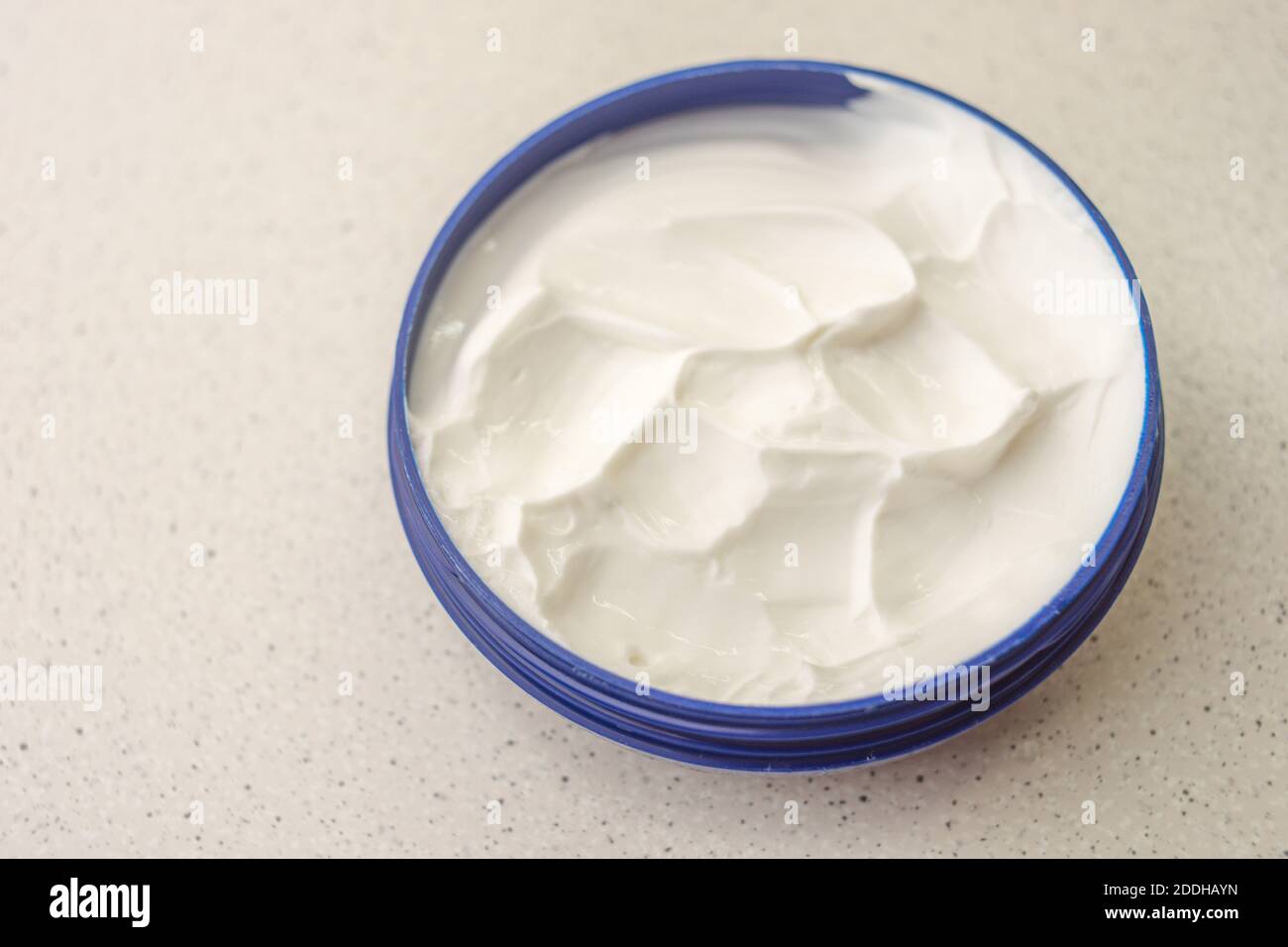 Aprire un contenitore blu con crema bianca su un tavolo di marmo. Foto Stock