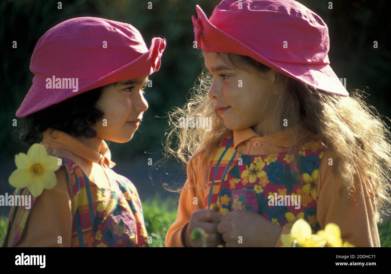 due sorelle in cappelli rosa faccia a faccia in giardino di narcisi Foto Stock
