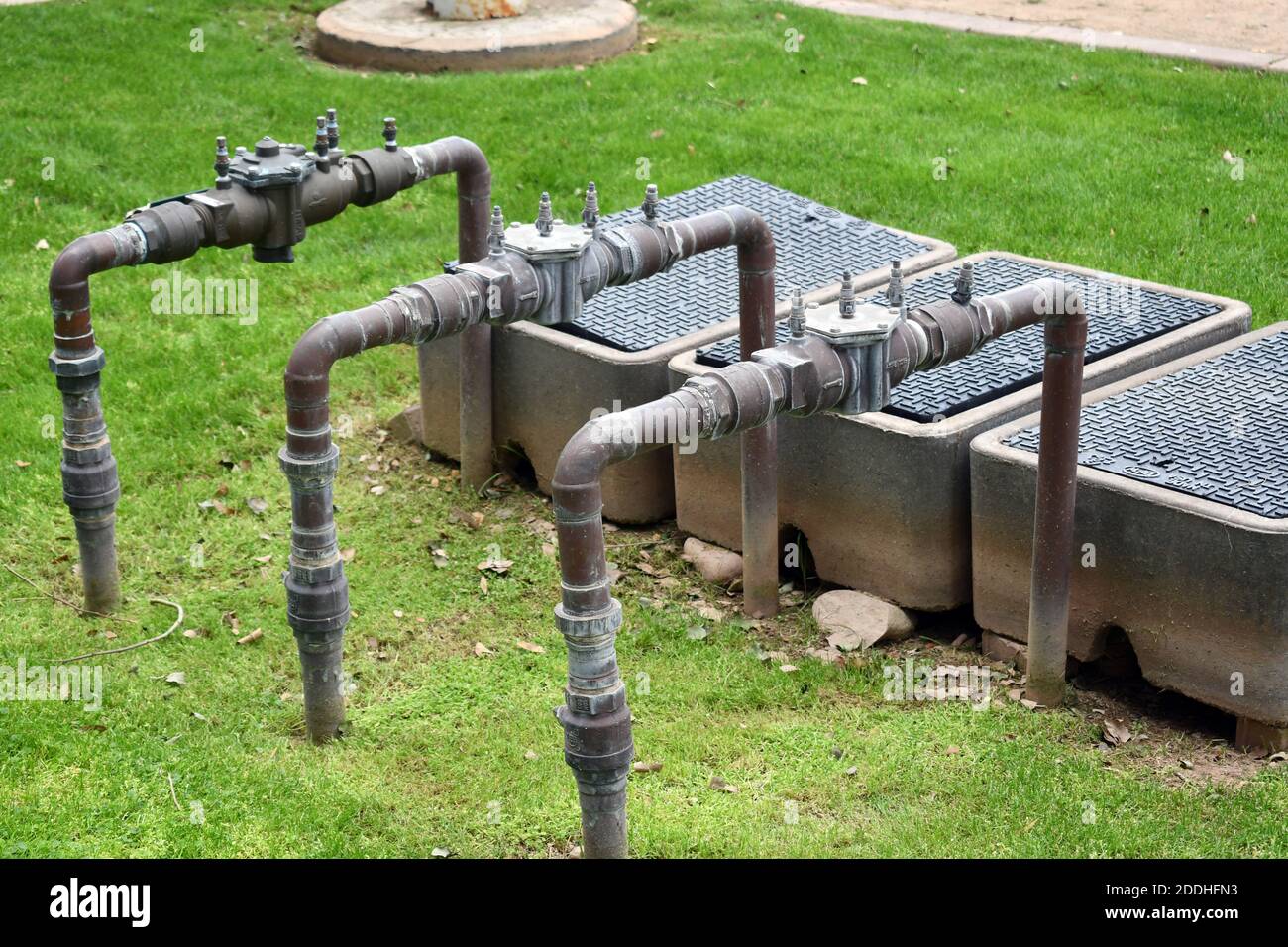 Un colpo di primo piano di condutture di approvvigionamento idrico in un giardino con un prato fresco coltivato Foto Stock