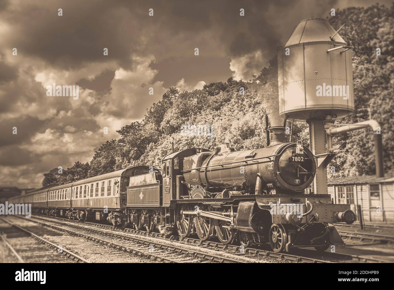 Vista laterale di Seppia di un treno a vapore d'epoca britannico che passa accanto alla torre dell'acqua a Bewdley, una delle stazioni di treni a vapore della Severn Valley. Foto Stock