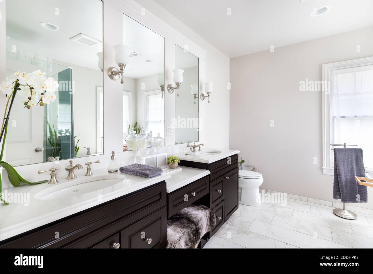 Una lussuosa stanza da bagno rimodellata con un vanity di legno scuro, decorazioni che si trovano sui piani di granito e pavimento in piastrelle di marmo. Foto Stock