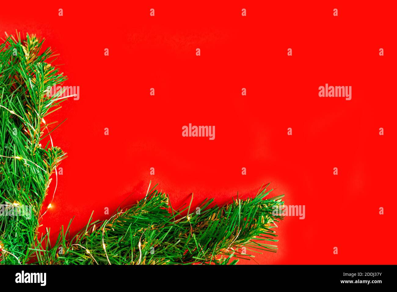 Rami di pino verde con lampadine su sfondo rosso incorniciano l'angolo dello sfondo natalizio, luci di vacanza, Foto Stock