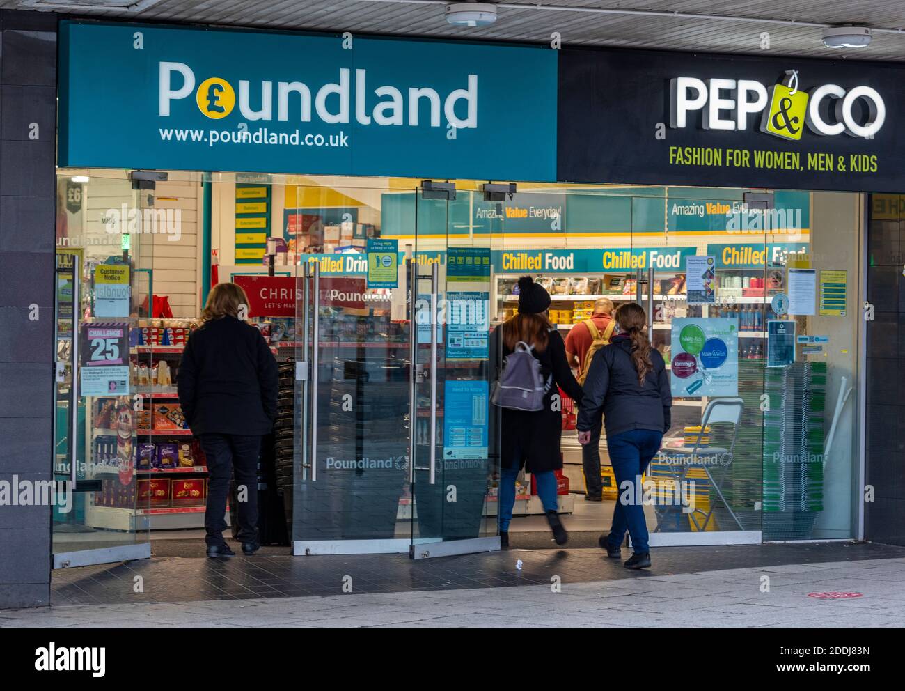 gli acquirenti che entrano in un ramo del centro cittadino di alta strada della catena di negozi al dettaglio di poundland con un grande marchio banner di poundland. Foto Stock