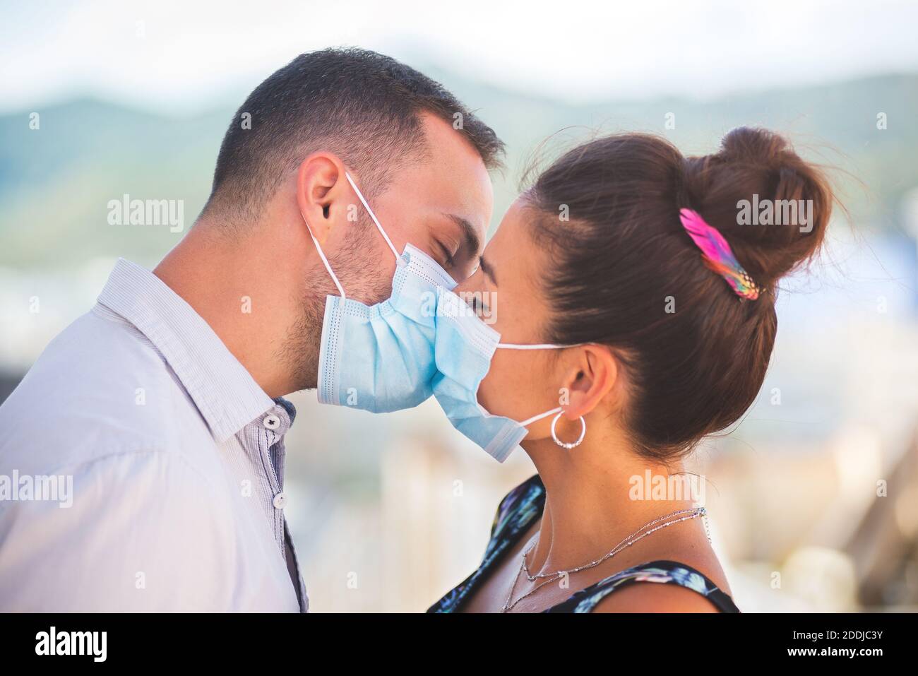 Un uomo e una donna si baciano con il coronavirus maschere di protezione Foto Stock