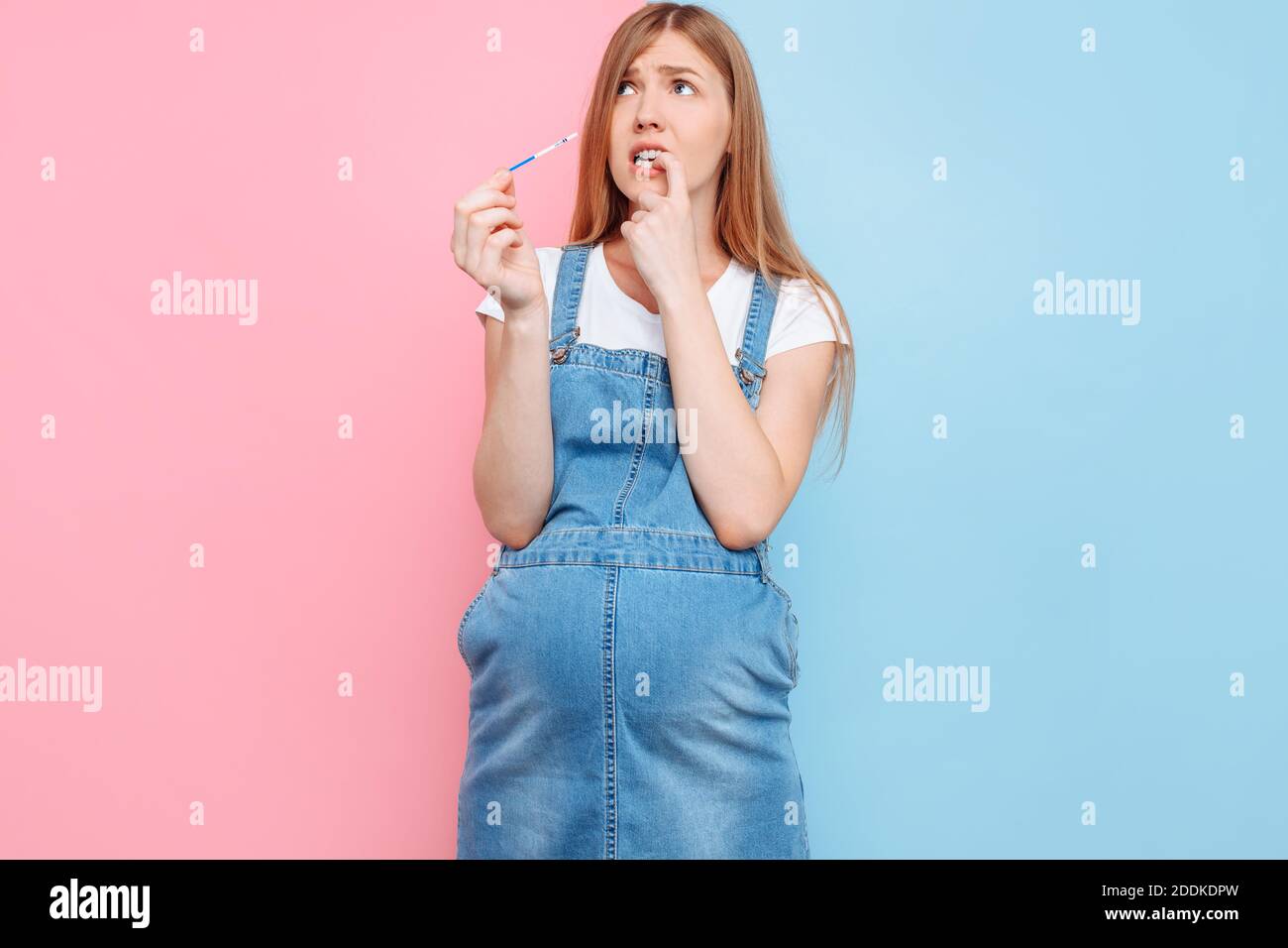 Sì, sono incinta UNA bella donna incinta scioccata mostra un risultato positivo di due strisce su un test, in piedi su una schiena rosa e blu isolata Foto Stock