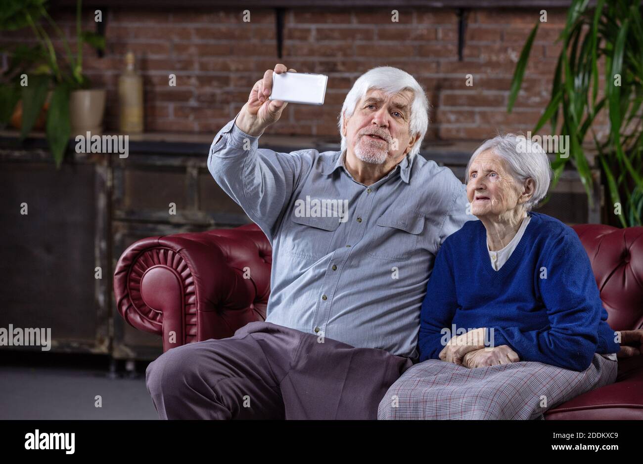 Coppia senior tenendo selfie con smart phone comodamente seduti sul divano di casa Foto Stock