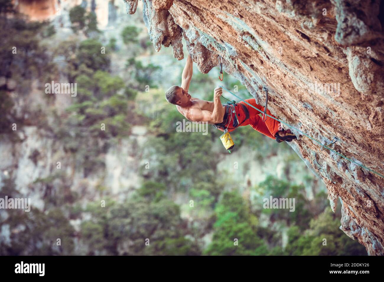 Scalatore di roccia che scalda la corda mentre si arrampica su un percorso impegnativo su una scogliera a strapiombo. Foto Stock