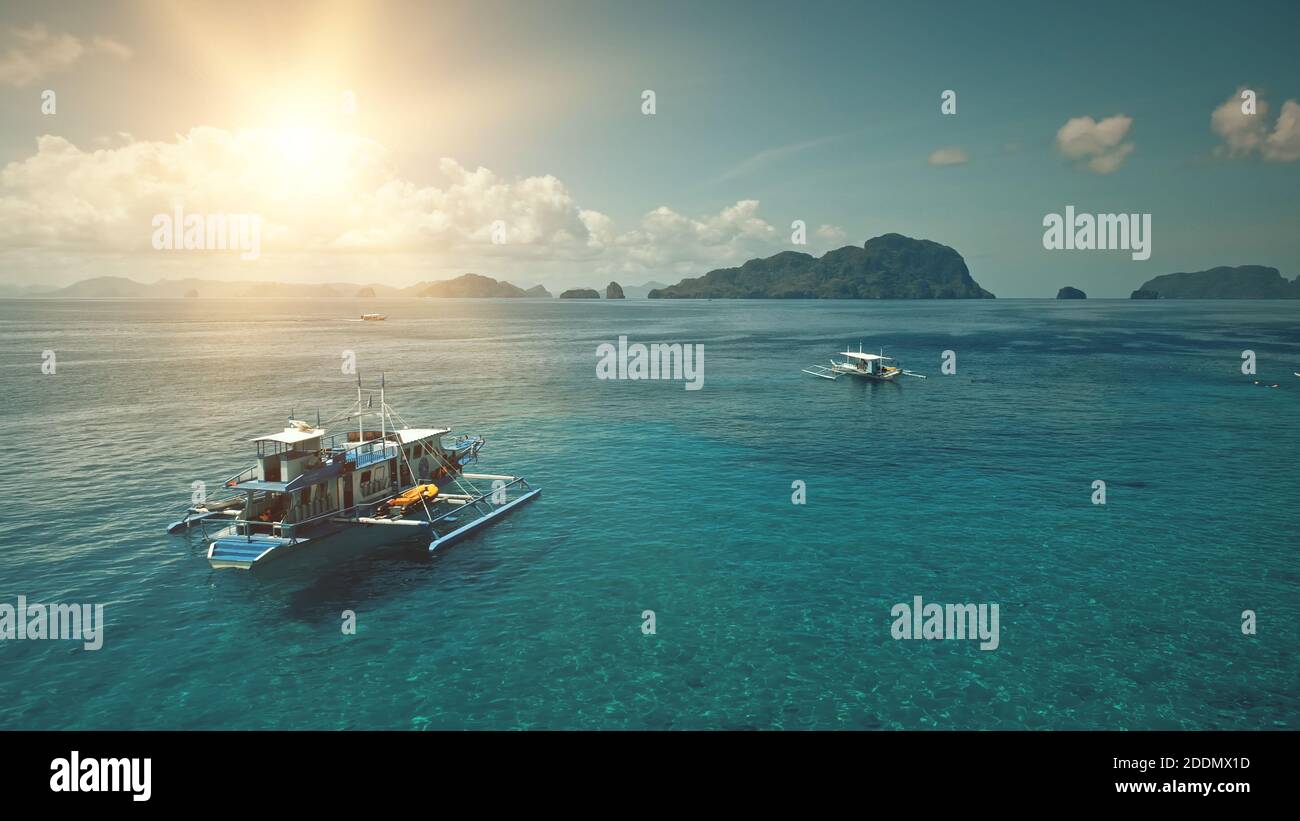 Barche sulla costa dell'oceano con il sole sopra la vista aerea dell'isola di montagna. Crociera nella baia con la verde montagna tropicale. La gente riposa sulla spiaggia di sabbia. Estate giornata di sole sull'isola di Palawan, Filippine, Asia Foto Stock