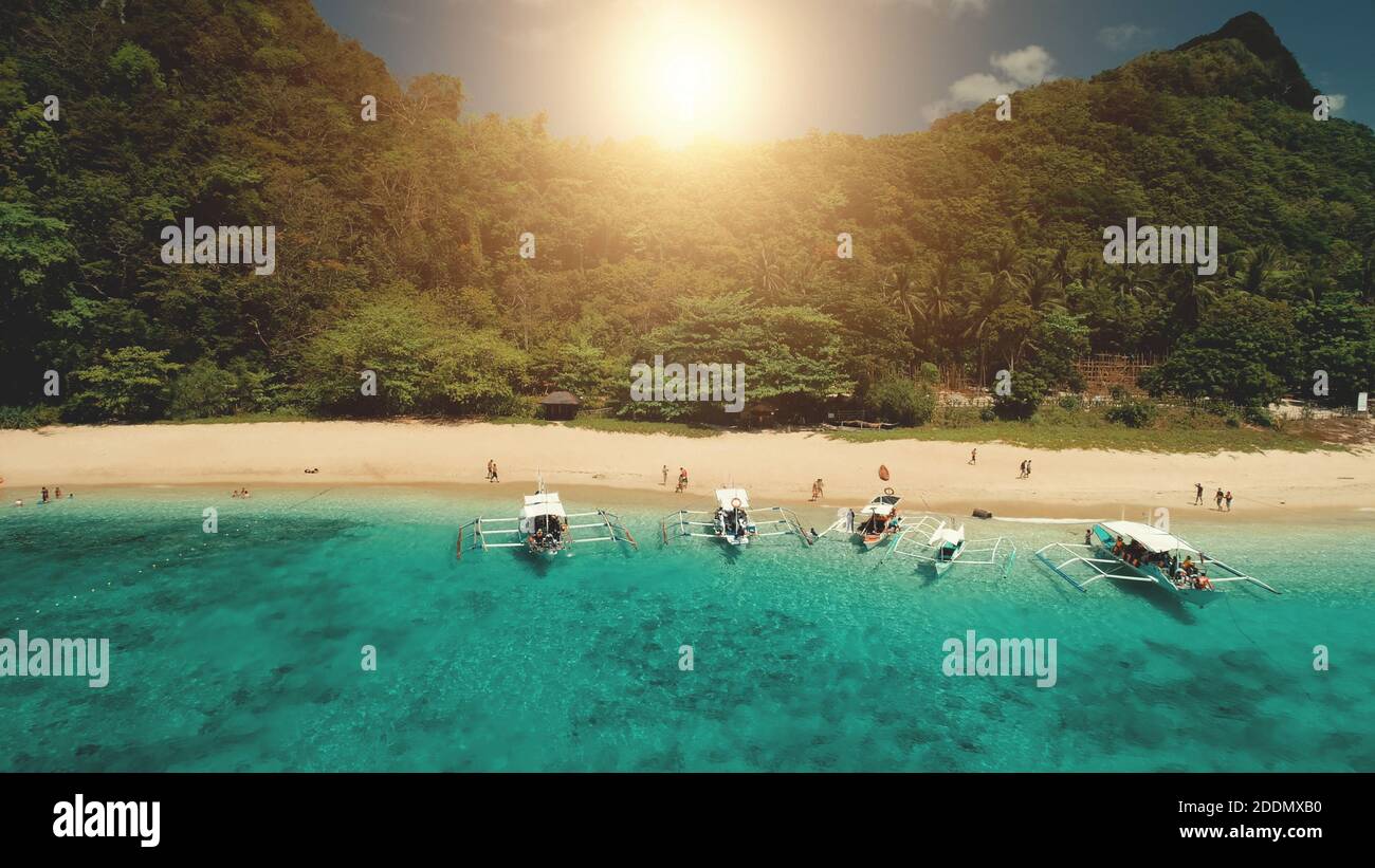 Barca per passeggeri vicino alla baia dell'oceano con una spiaggia rocciosa verde durante la crociera estiva di un giorno di sole. Mare tropicale all'isola di montagna di El Nido, Filippine, arcipelago di Visayas. Primo piano cinematografico con drone shot Foto Stock
