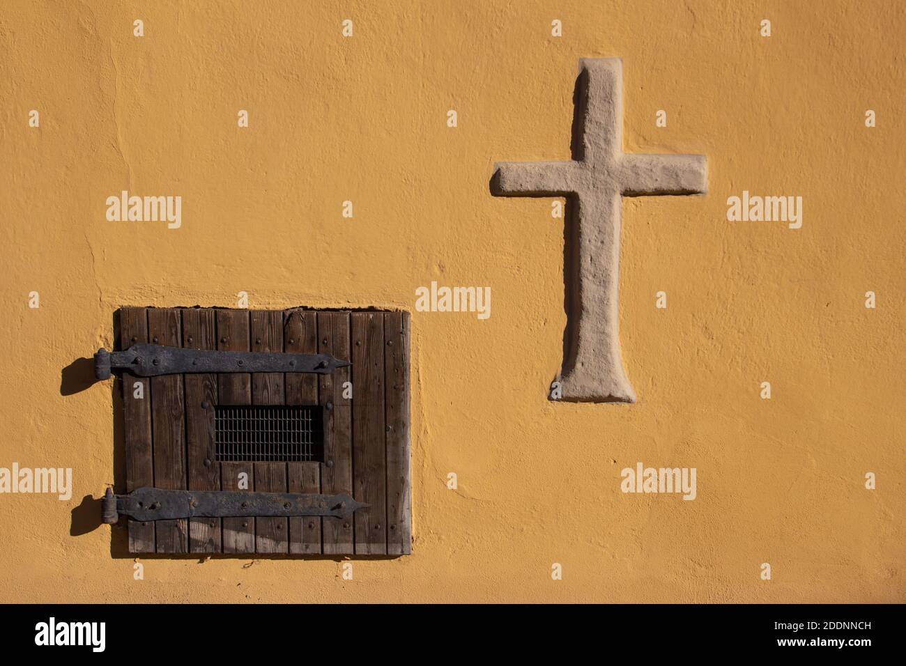 Vecchia tapparella in legno vintage con griglia metallica e un naturale croce di pietra su un muro giallo Foto Stock