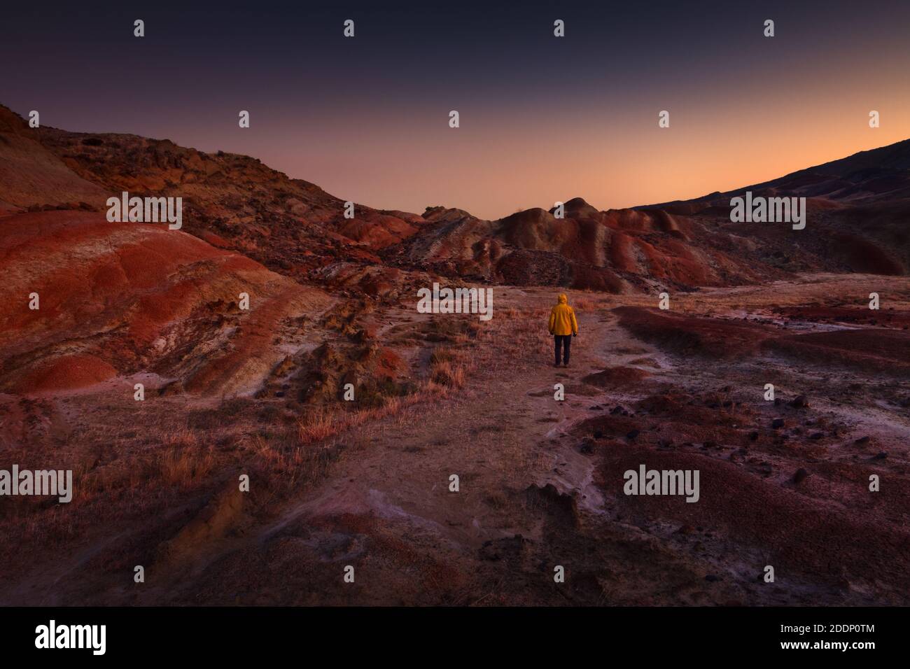 Tramonto a Udabno, regione di Kakheti, Georgia, confine con l'Azerbaigian. Un escursionista solitario con una giacca gialla si erge in mezzo a un terreno desertico accidentato e colorato. Foto Stock
