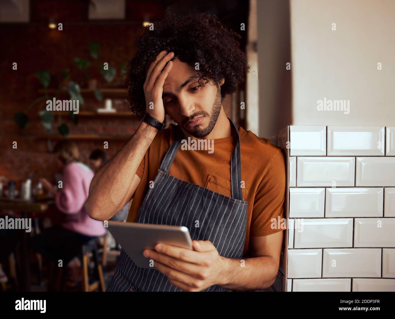 Giovane uomo serio proprietario di caffè usando il tablet digitale mentre in piedi appoggiandosi alla parete Foto Stock