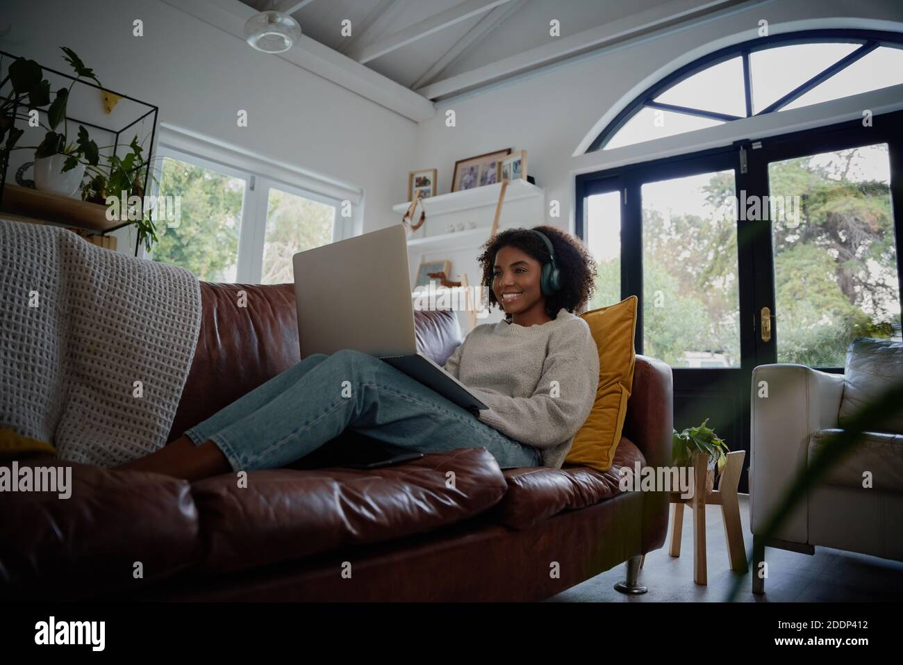Ragazza felice che indossa le cuffie per guardare e ascoltare i video sul computer portatile seduto sul divano a casa Foto Stock
