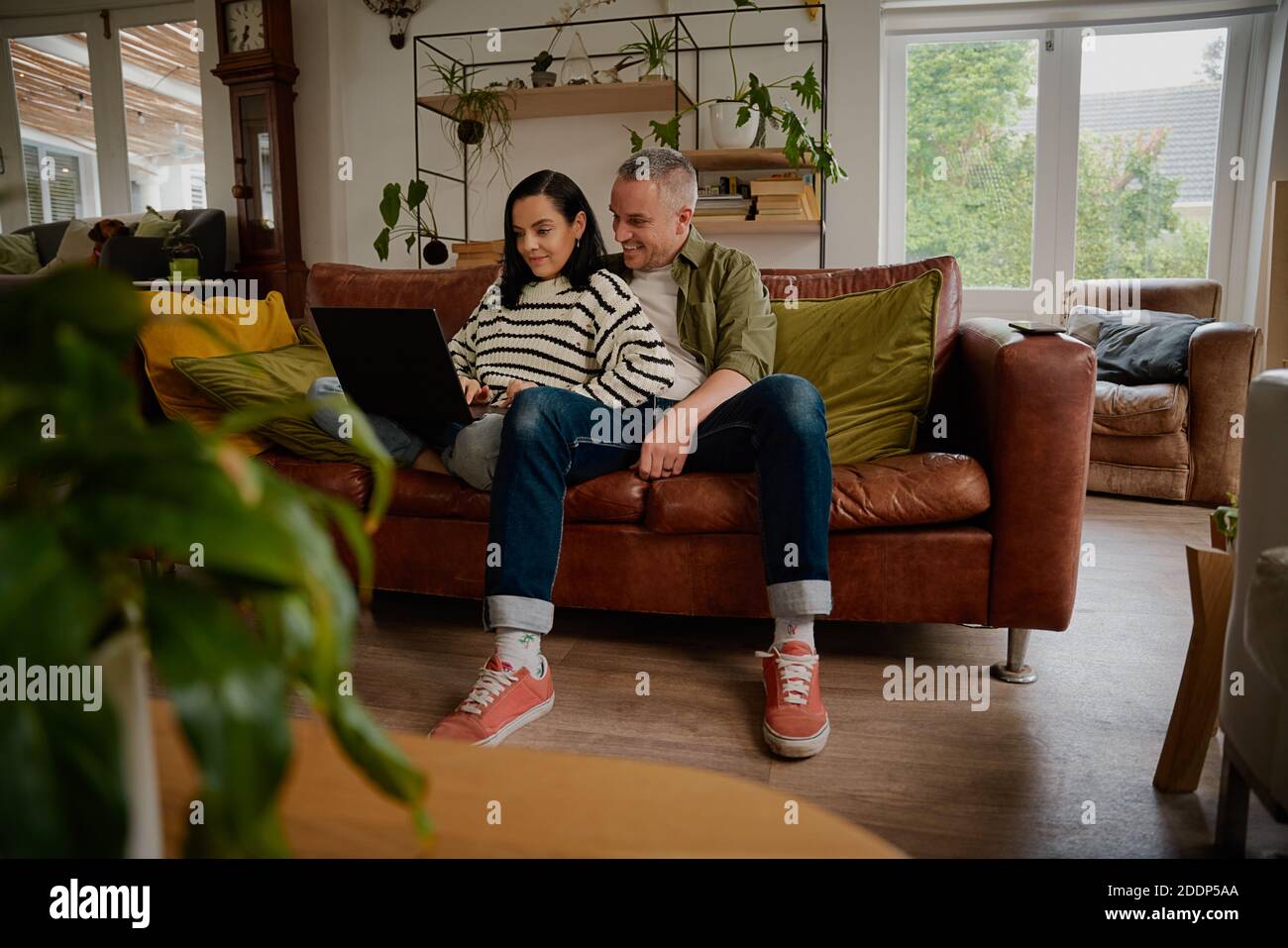Giovane donna che naviga i siti di shopping sul computer portatile mentre si è seduti con marito a casa Foto Stock