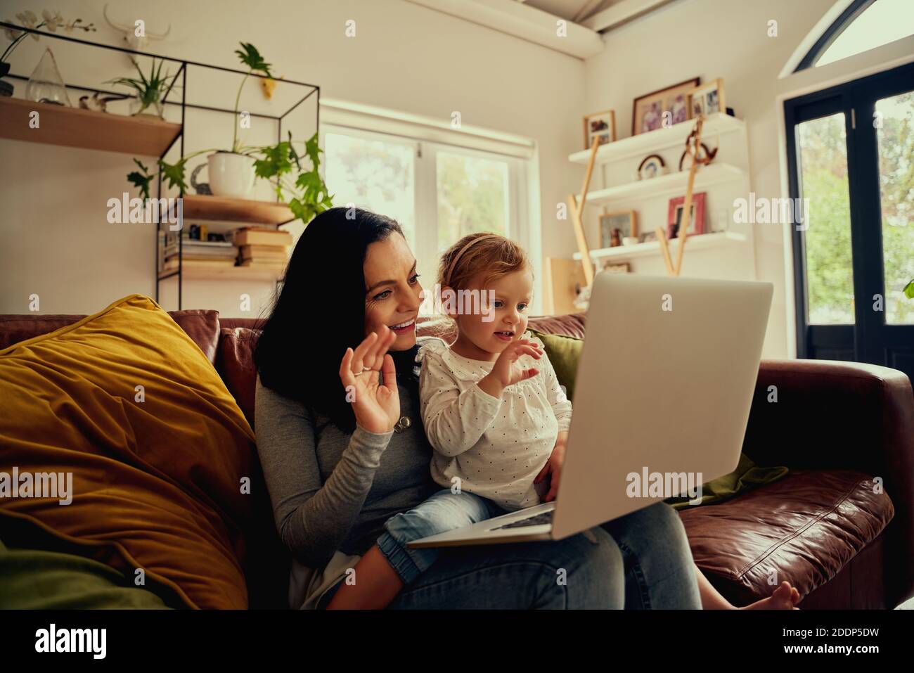 Bella giovane madre con carina piccola figlia che fa la videochiamata utilizzo di un computer portatile a casa seduto sul divano Foto Stock