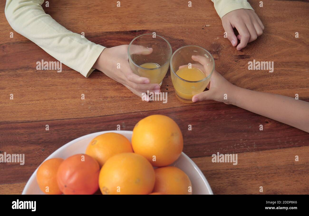 bambino che tiene un bicchiere di succo di frutta d'arancia promuovere un'alimentazione sana su un tavolo foto di scorta Foto Stock
