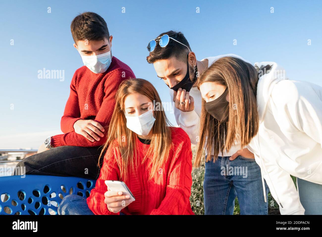 Gruppo di giovani amici che guardano lo smartphone all'aperto Maschera di protezione sicura per coronavirus - due coppie eterosessuali di viaggiatori ricerca onl Foto Stock