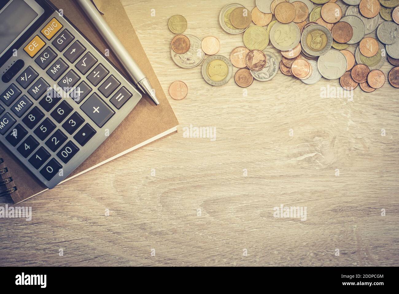 Soldi (monete), calcolatrice e qualche cancelleria su tavolo di legno, vista dall'alto con copy space - concetto di fondo finanziario Foto Stock