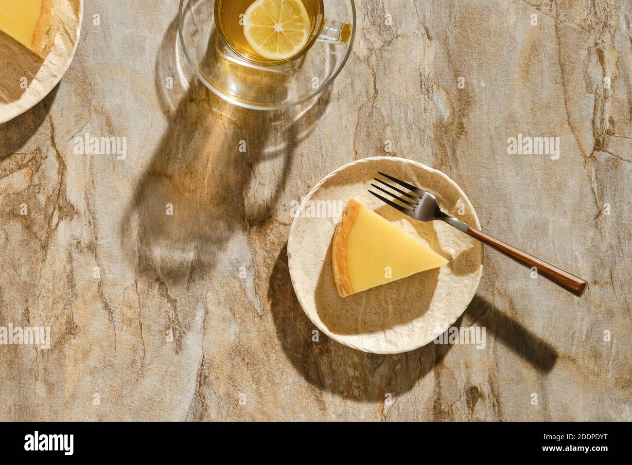 Vista dall'alto di un pezzo di torta al limone con tè sotto luce solare diretta con ombre dure sul tavolo Foto Stock