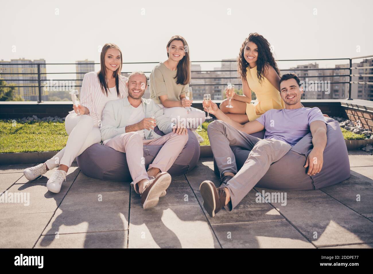 Foto di buon umore sorridente felice allegro gruppo positivo di gli amici siedono sulla poltrona, bevono champagne all'esterno sul tetto Foto Stock