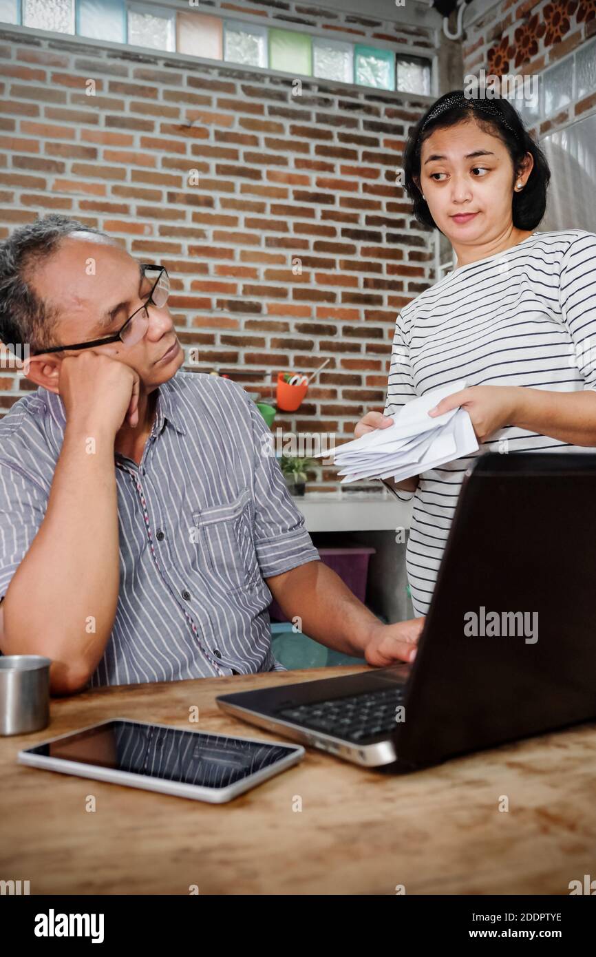 Stile di vita domestico del sud-est asiatico, moglie che consegna le fatture mensili mentre suo marito sembra riluttante, pensando al loro commercio Foto Stock