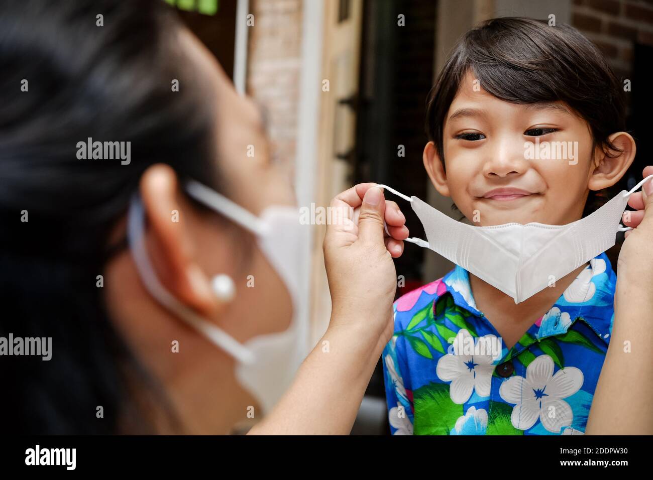 Madre del sud-est asiatico che aiuta il bambino usando la maschera di faccia Foto Stock