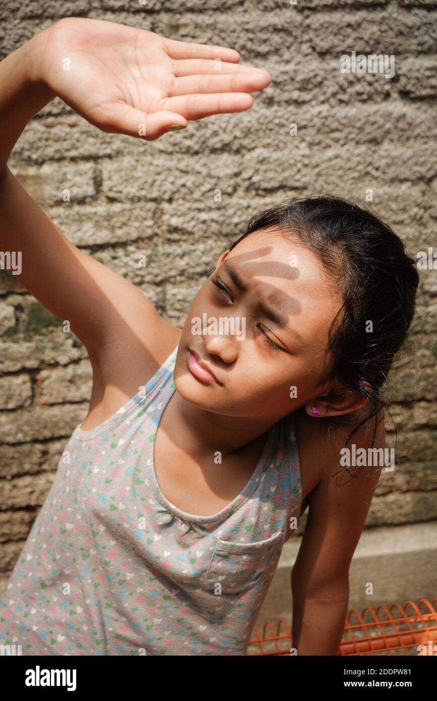Etnia del sud-est asiatico adolescente ragazza all'aperto prendere il sole al mattino a casa. Mano che si alza per coprire il viso dalla luce solare dura Foto Stock