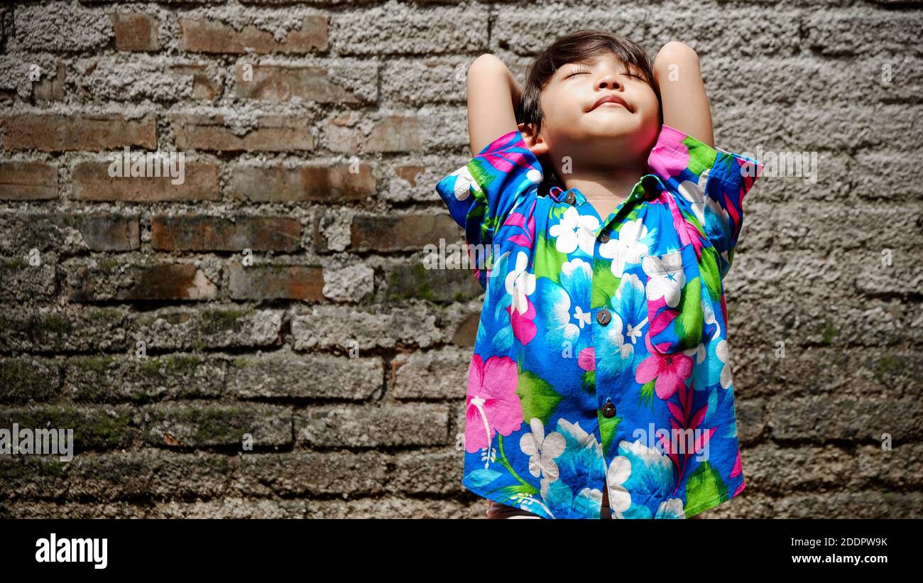 Felice bambino etnico del sud-est asiatico che si diverte a prendere il sole la mattina in cortile a casa Foto Stock