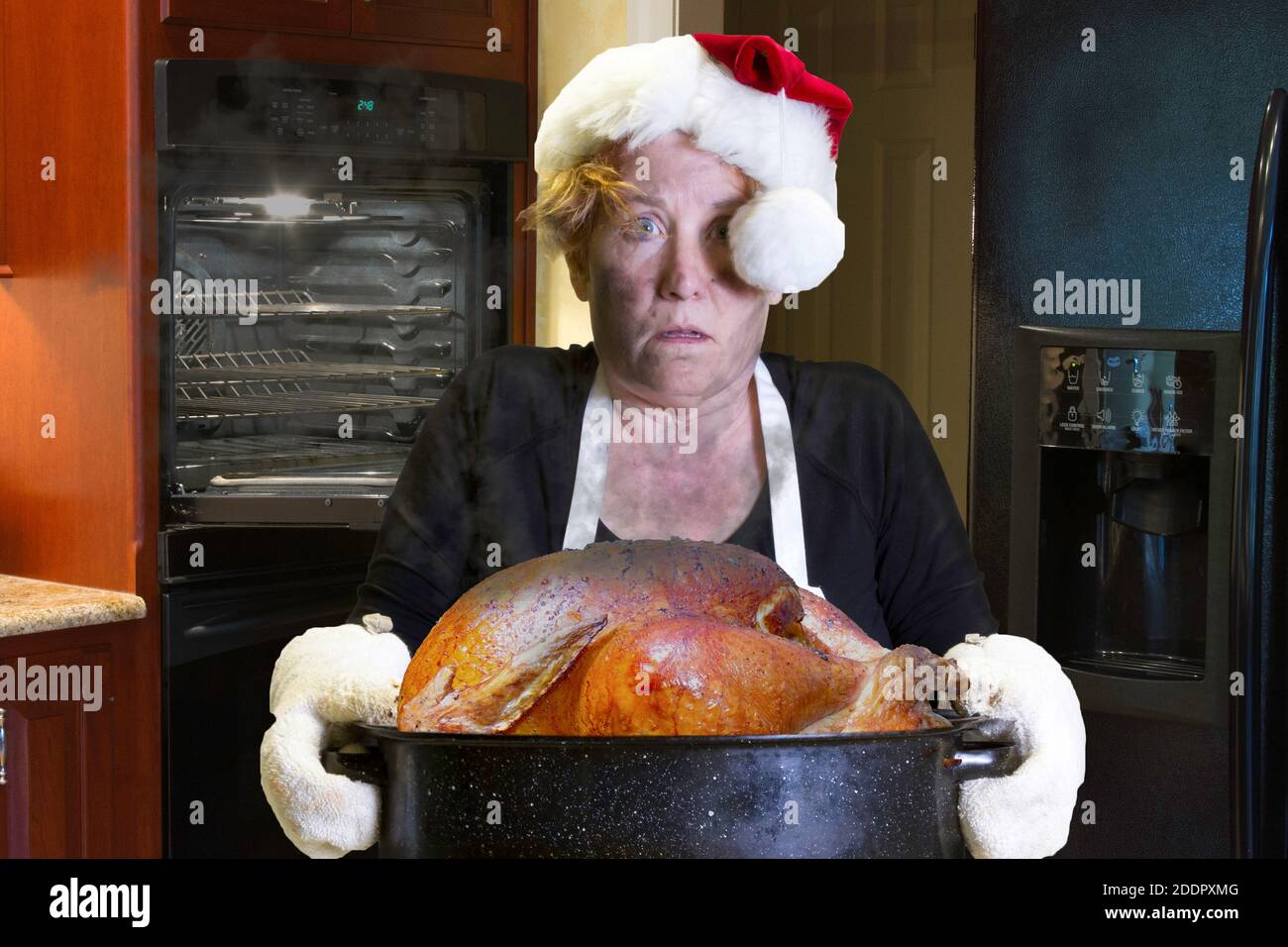 Donna in grembiule con calza di Natale hat holding teglia con faccia carbonizzati e sconvolto l'espressione in cucina. Foto Stock